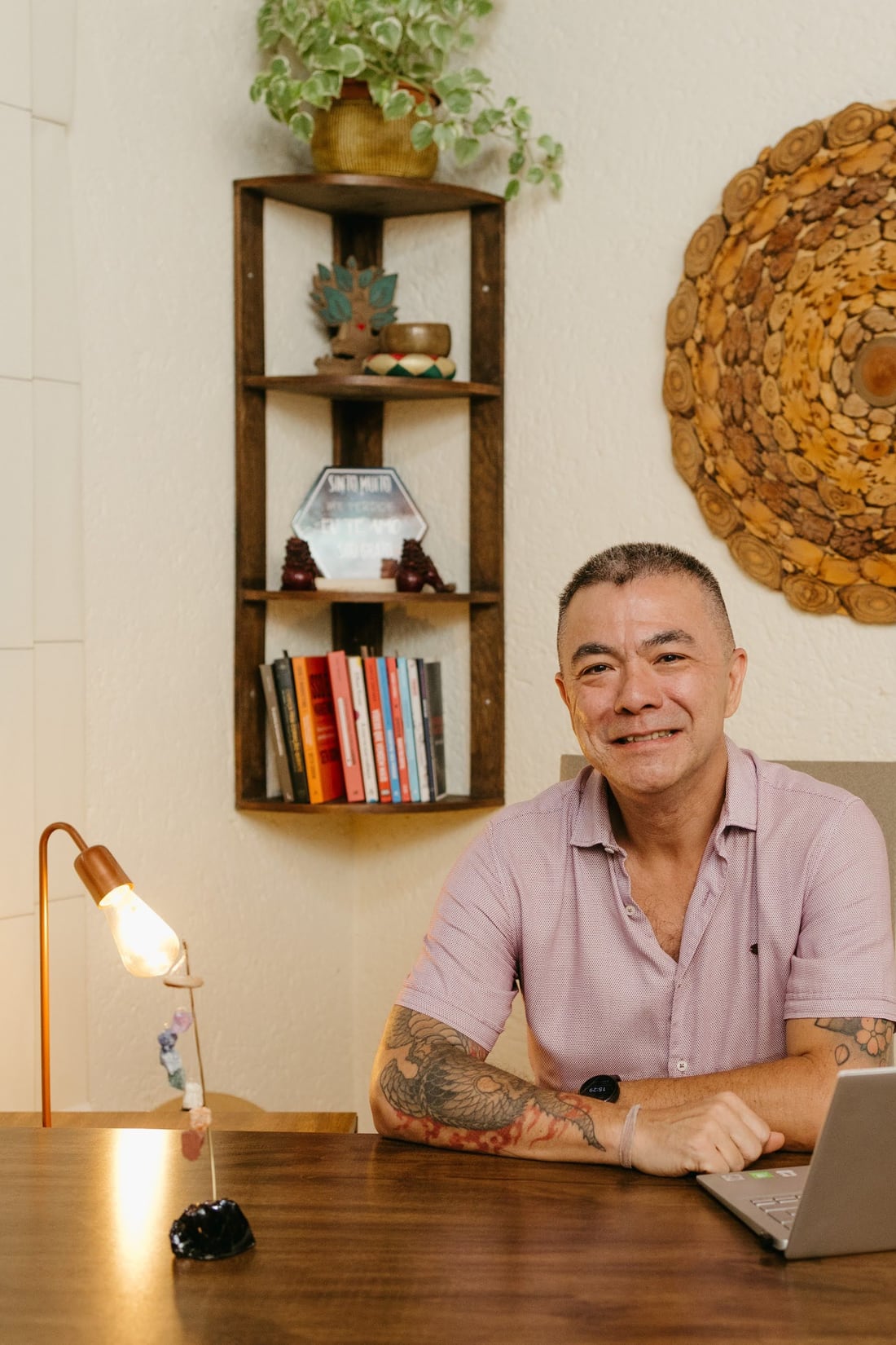 Alex Possato sorrindo, sentado à mesa de trabalho com o notebook
