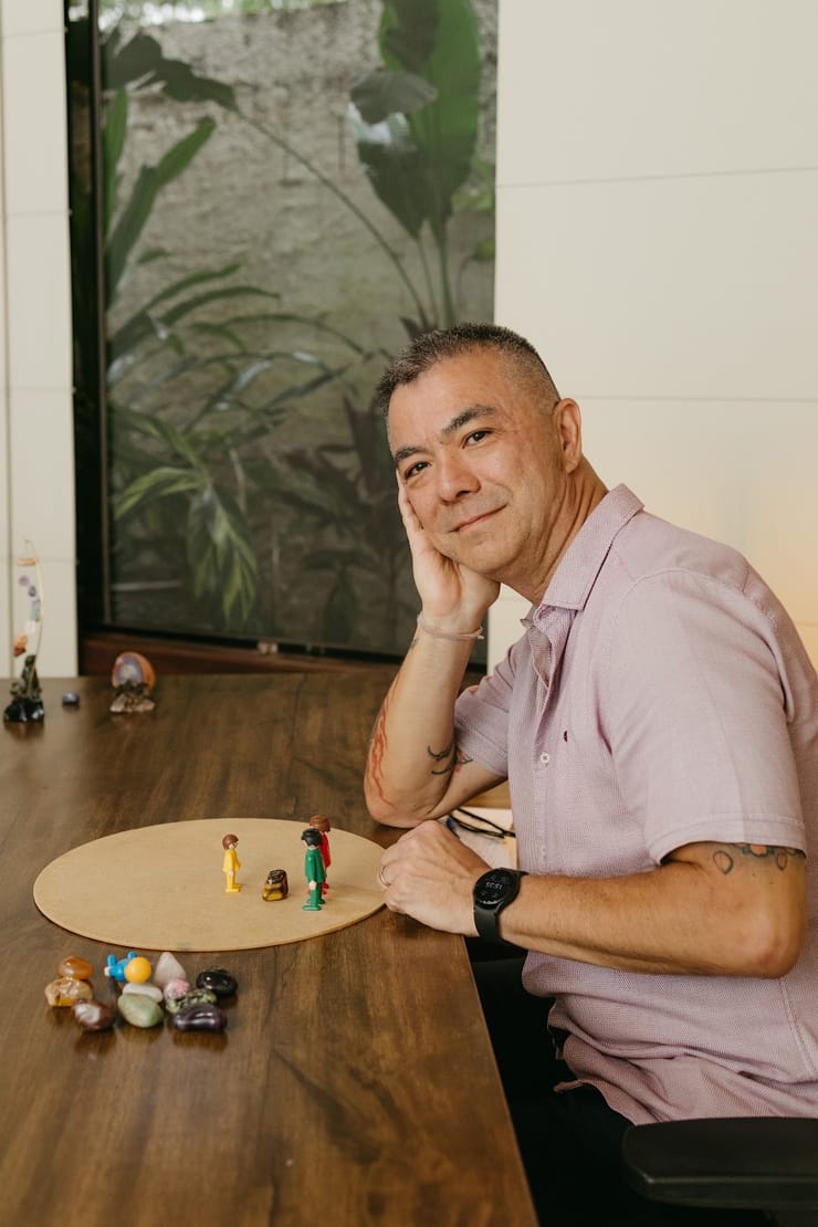 Alex Possato acolhedor junto à janela, com os bonecos sobre a mesa